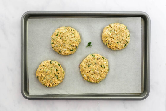 Four salmon burger patties shaped on a sheet pan lined with parchment paper.
