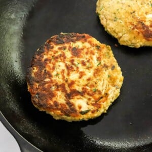 Two salmon burgers cooking in a cast iron skillet.