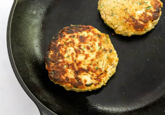 Two salmon burgers cooking in a cast iron skillet.