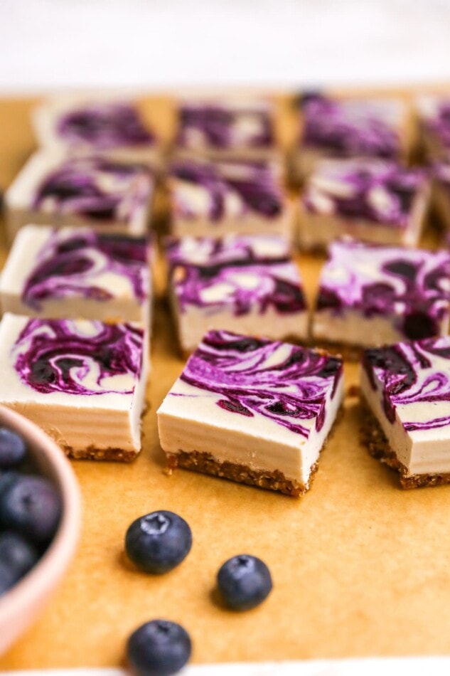 Vegan blueberry cheesecake bars on a sheet of parchment paper.