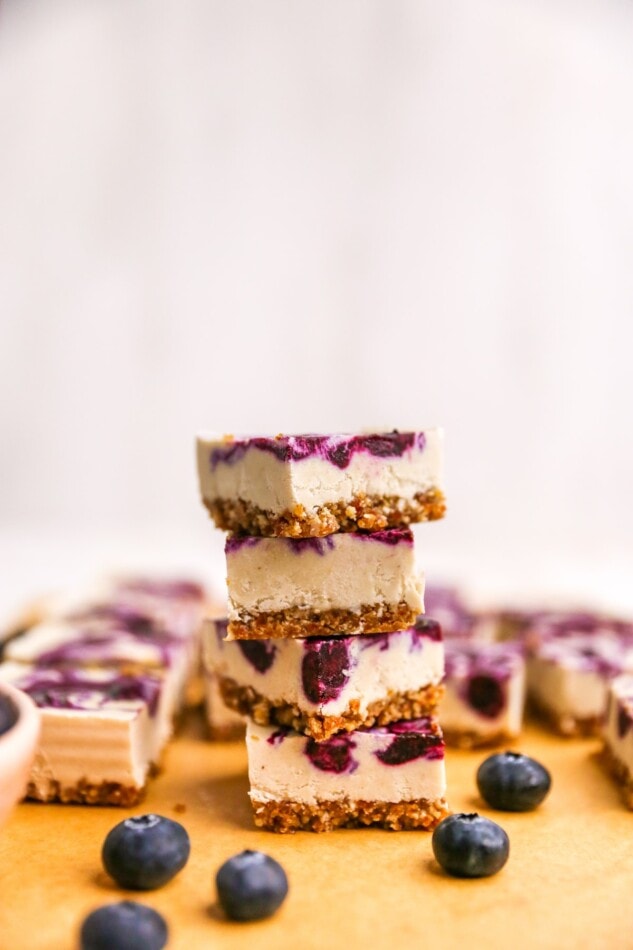 Four vegan blueberry cheesecake bars stacked on top of each other.