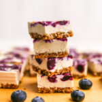Four vegan blueberry cheesecake bars stacked on top of each other.