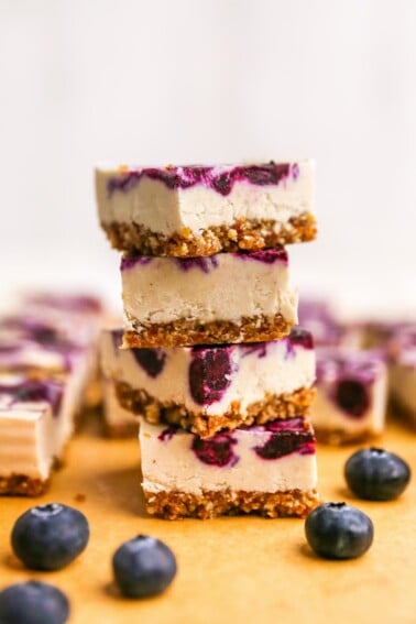 Four vegan blueberry cheesecake bars stacked on top of each other.