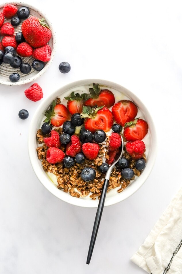 Berries, granola and honey yogurt bowl with a spoon.
