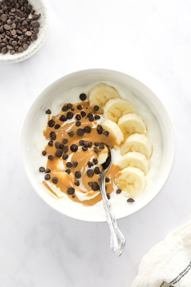 Chunky monkey yogurt bowl with banana, chocolate chips and peanut butter with a spoon.