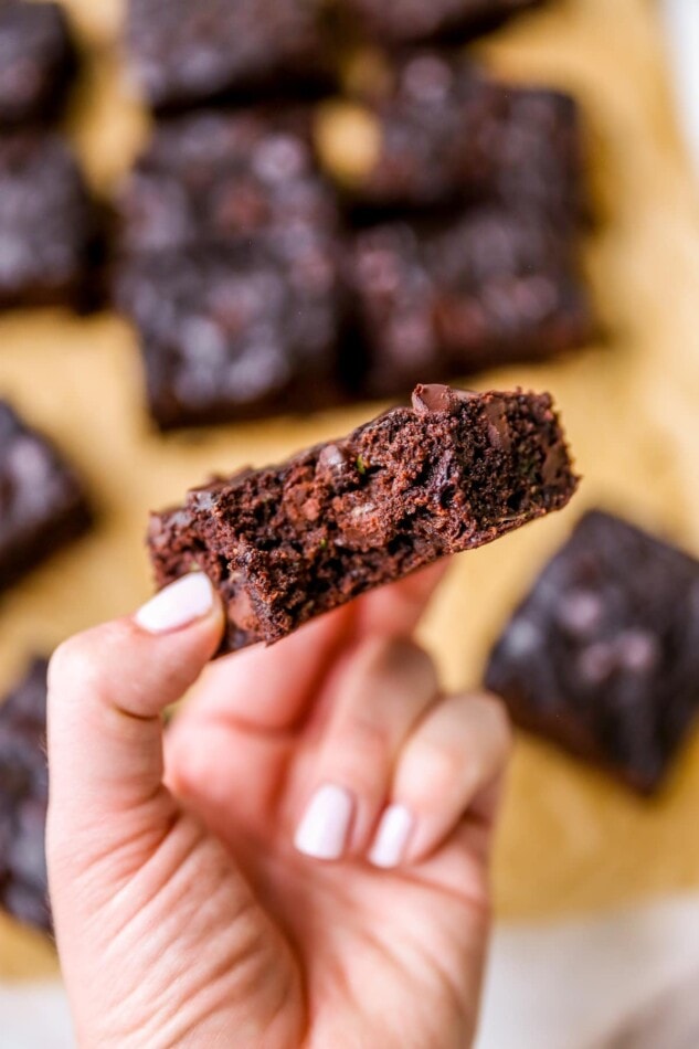 Hand holding a zucchini brownie with a bite taken out of it.