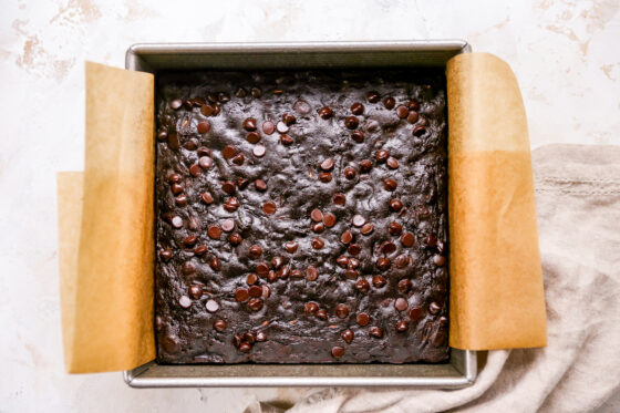 Baked zucchini brownies in a square baking pan lined with parchment paper.