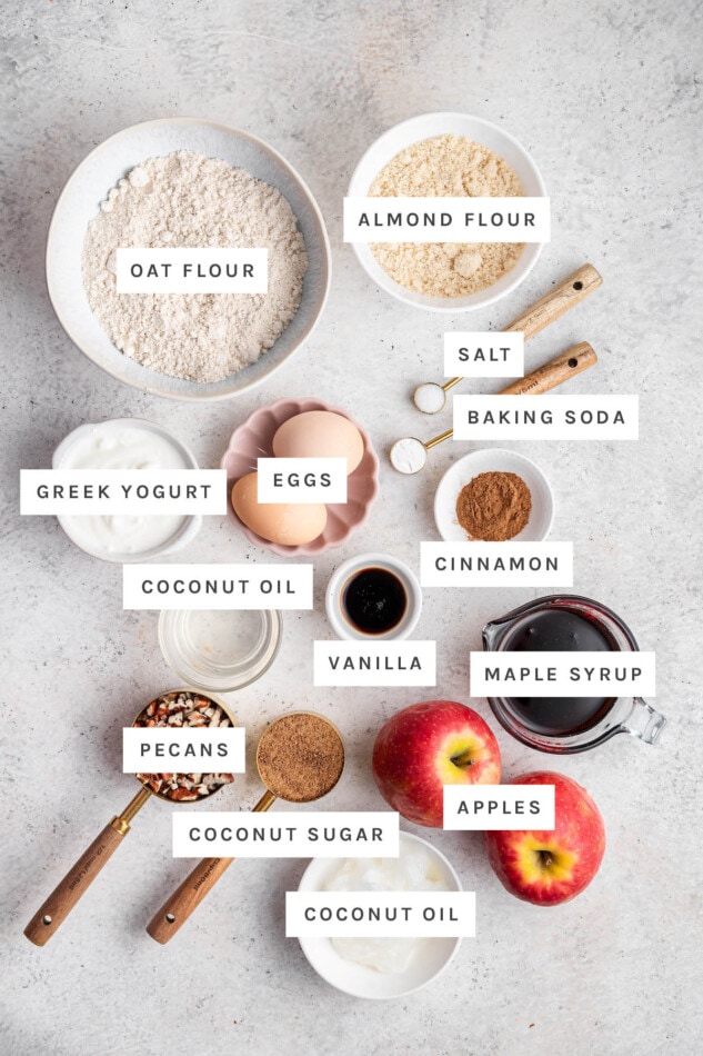 Ingredients measured out to make an apple cake: oat flour, almond flour, salt, baking soda, eggs, Greek yogurt, cinnamon, coconut oil, vanilla, maple syrup, pecans, coconut sugar and apples.