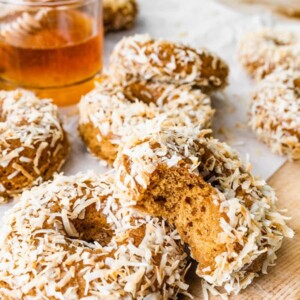 Donuts coated in toasted coconut. One donut has a bite taken out of it.