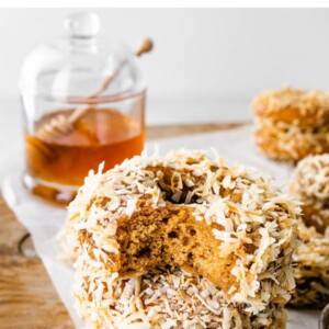 Stack of three coconut donuts. The top has a bite taken out of it.