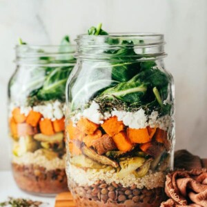 Two mason jars with ingredients layered to make kale sweet potato lentil salads.
