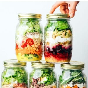 Hand stacking five different mason jar meal prep salads.