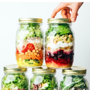 Hand stacking five different mason jar meal prep salads.