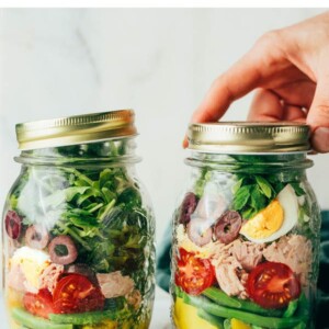 Two mason jars with meal prep tune nicoise salads layered in them.
