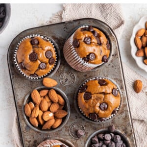 Protein muffins in a muffin tin, some of the cavities contain chocolate chips and almonds instead of a muffin.