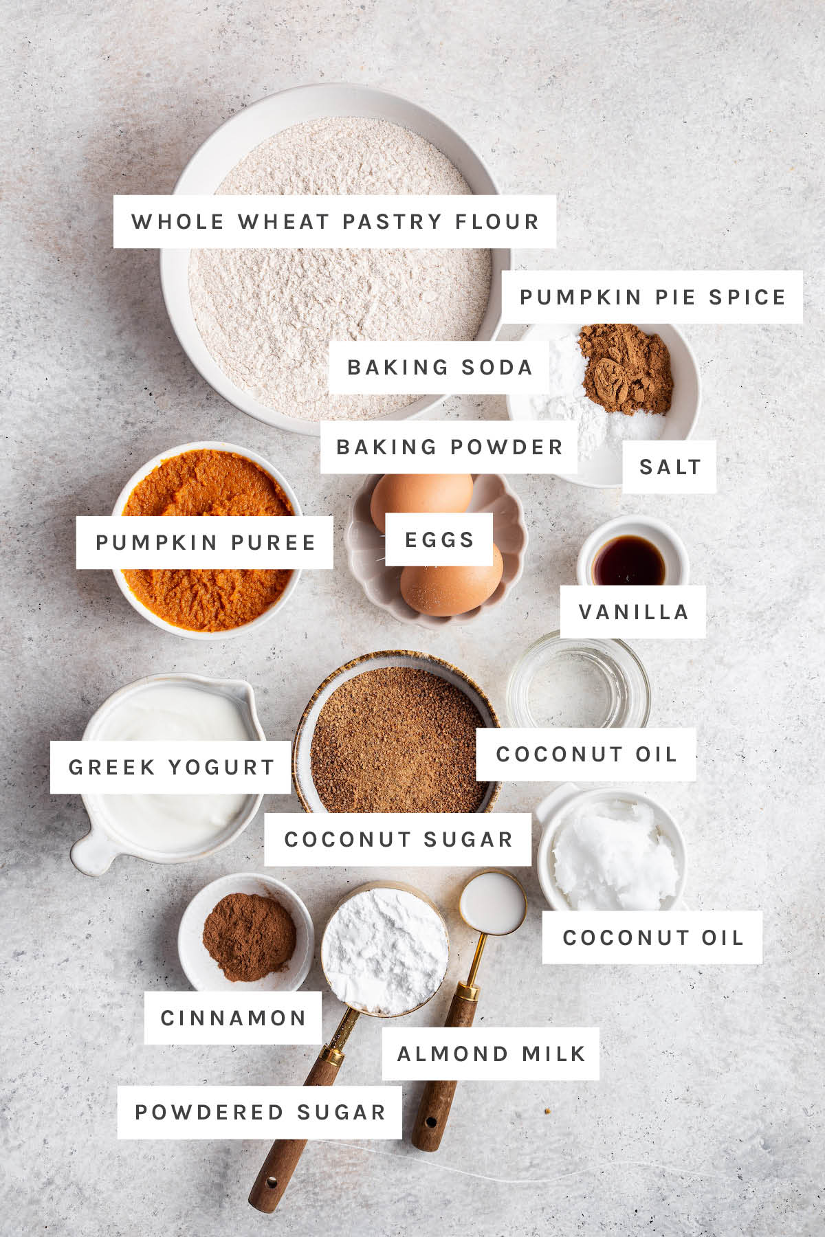Ingredients measured out to make pumpkin coffee cake: whole wheat pastry flour, pumpkin pie spice, baking soda, baking powder, salt, eggs, pumpkin puree, vanilla, coconut oil, coconut sugar, Greek yogurt, cinnamon, powdered sugar and almond milk.