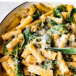 Pumpkin pasta in a pot topped with fresh sage, cheese and pepitas.