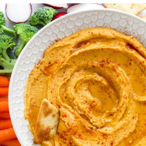 Close up of sweet potato hummus in a bowl. A pita chip rests in the hummus.