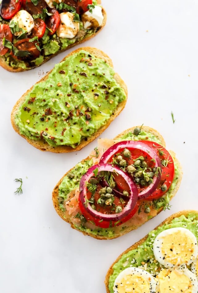Four styles of avocado toast laid diagonally across the photo frame.