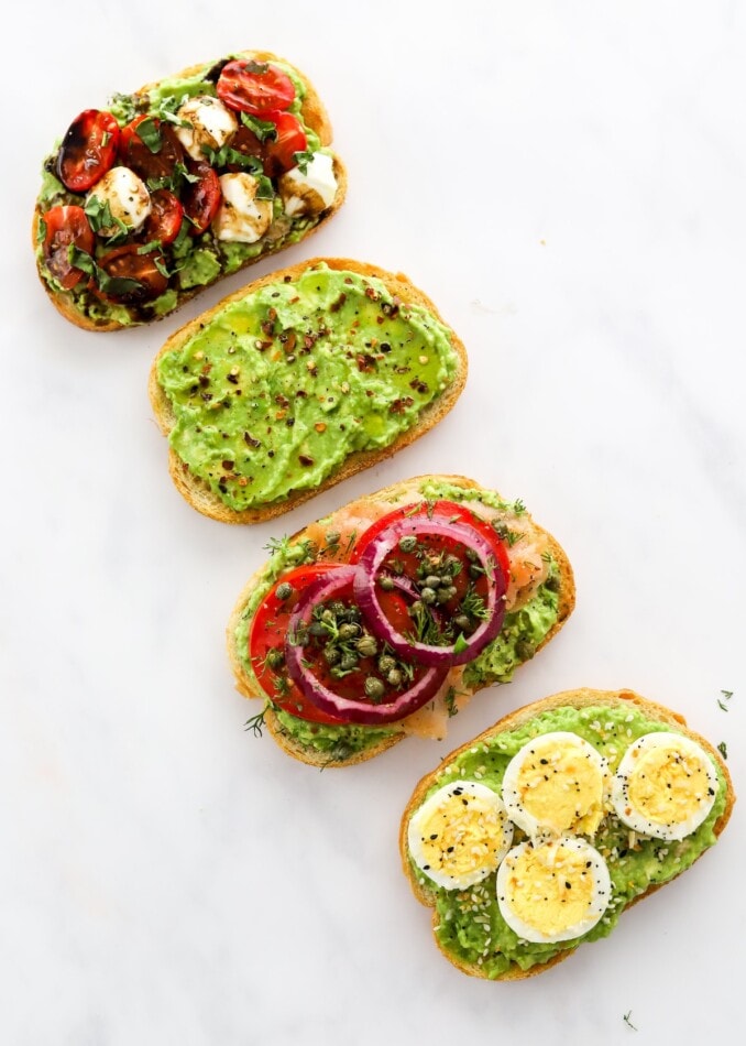 Four styles of avocado toast laid diagonally across the photo frame.
