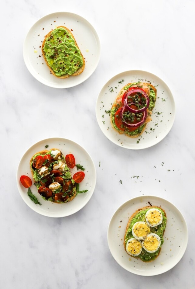 Four styles of avocado toast on four plates.