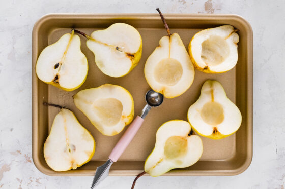 Halved pears with a melon baller that has scooped out a shallow hole in the pears.