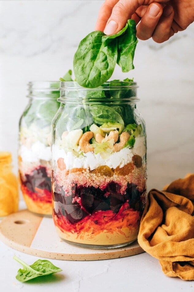 Adding spinach to a jar containing ingredients for beet power salad.