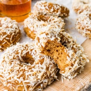 Coconut crunch donuts scattered across a cutting board, one donut has a bite removed.