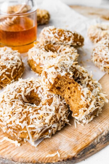 Coconut crunch donuts scattered across a cutting board, one donut has a bite removed.