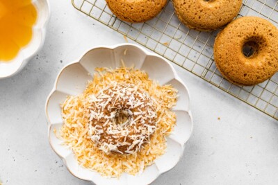 A donut, after being dipped into honey, now dipped in toasted coconut flakes.