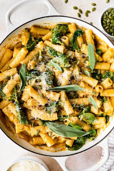 Creamy pumpkin pasta in a pot topped with fresh sage, pepitas and cheese.