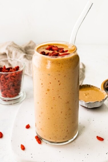 A butterfinger smoothie in a glass with a straw topped with goji berries.
