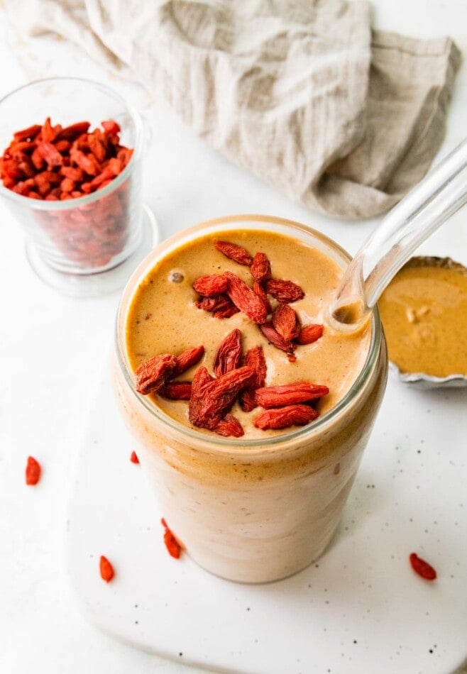 A glass with a straw containing healthy butterfinger smoothie topped with goji berries.