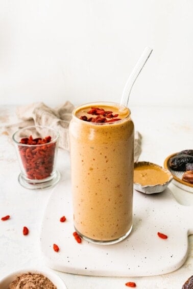 A butterfinger smoothie in a glass with a straw topped with goji berries.