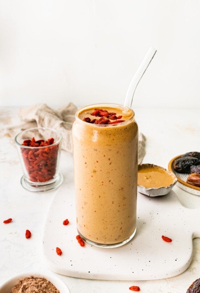 A butterfinger smoothie in a glass with a straw topped with goji berries.