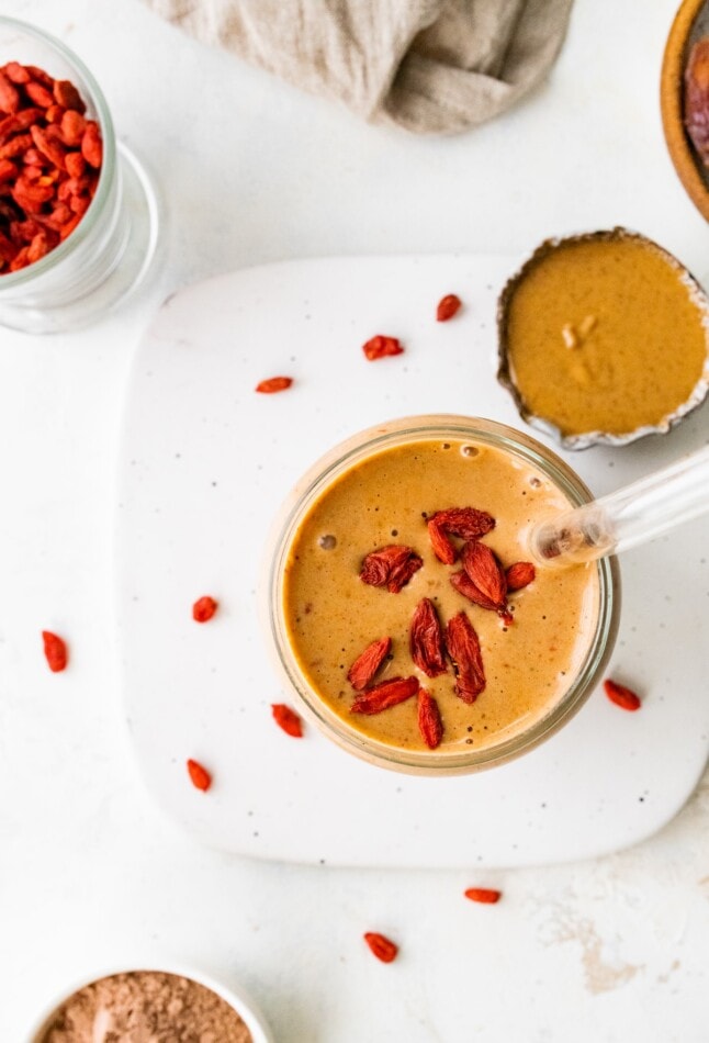 Overhead view of a glass of butterfinger smoothie with a straw topped with goji berries.