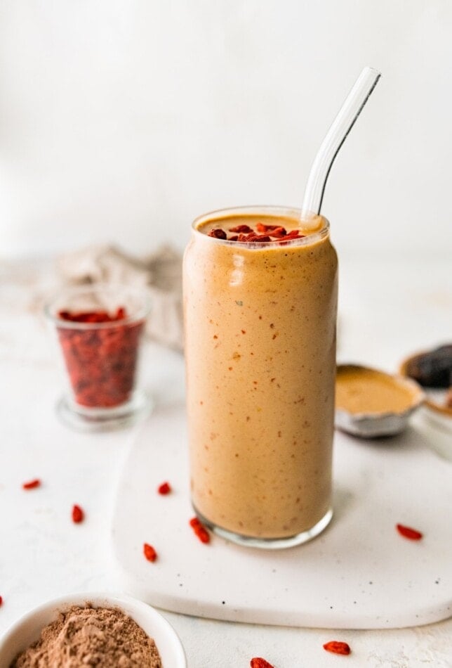 A glass with a straw containing healthy butterfinger smoothie topped with goji berries.