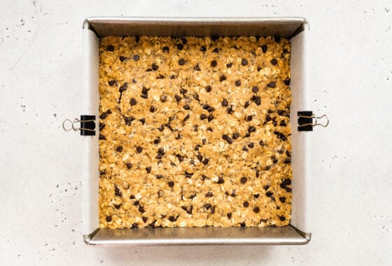 Peanut butter protein bar mixture in a square baking pan lined with parchment paper.