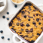 Protein baked oatmeal in a baking dish with bowls of blueberries and oats around it.
