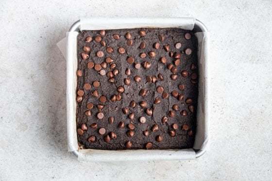 Baked pumpkin brownies in a square baking pan lined in parchment paper.