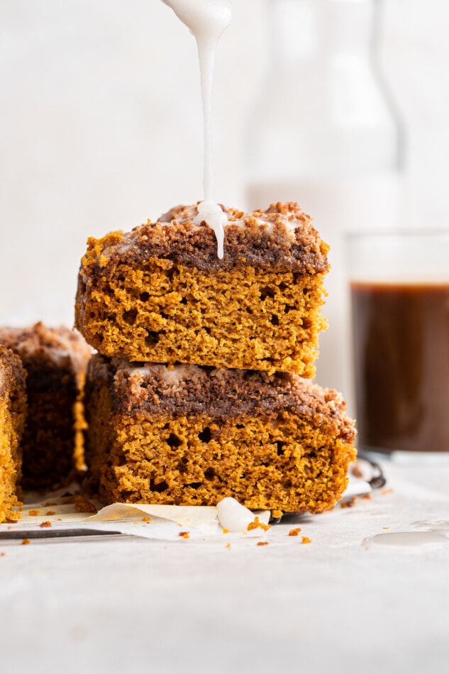 Drizzling extra icing over a stack of two slices of pumpkin coffee cake.