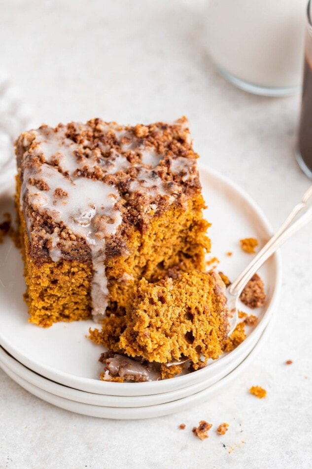 A square of pumpkin coffee cake on a plate, a fork has a bite resting on it.