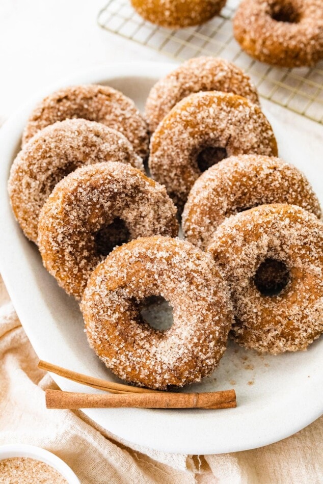 Pumpkin spice donuts on a serving platter with extra cinnamon sticks.