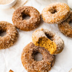 Pumpkin spice donuts on a sheet of parchment paper. Two donuts are resting against each other and the top one has a bite missing.