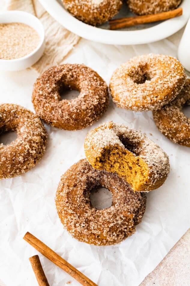 Pumpkin spice donuts on a sheet of parchment paper. Two donuts are resting against each other and the top one has a bite missing.