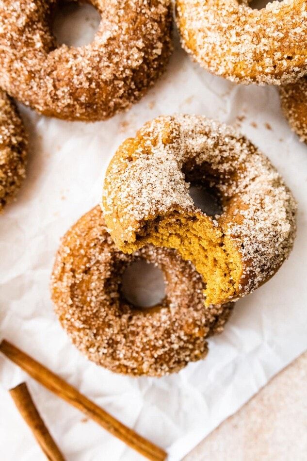 Two pumpkin spice donuts leaning against each other, the top donut has a bite removed.