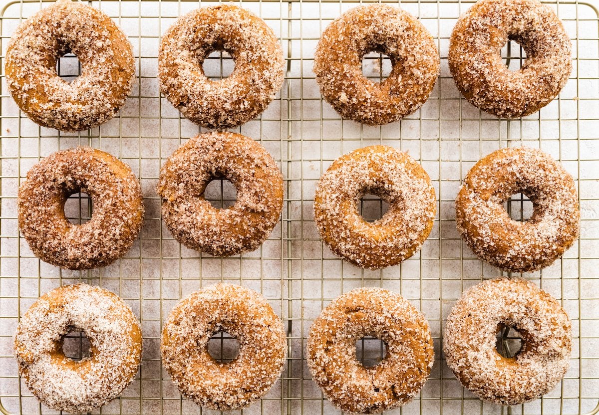 Twelve pumpkin spice donuts on a wire cooling rack.