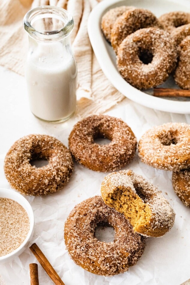 Donuts on a sheet of parchment paper with a jug of milk.