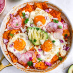 Overhead view of red chilaquiles with egg and avocado in a pan.