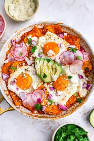 Overhead view of red chilaquiles with egg and avocado in a pan.